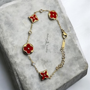 May include: Gold-toned bracelet featuring alternating red flower and diamond-shaped charms. The bracelet includes clear crystal accents and a lobster clasp closure. The jewelry is displayed on a light gray surface.