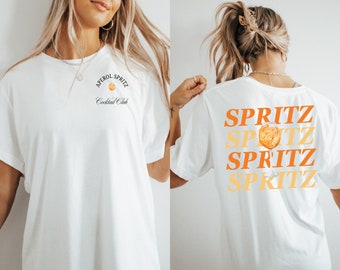 May include: White t-shirt with a graphic of a glass of Aperol Spritz and the text "Aperol Spritz Cocktail Club" on the front. The back of the shirt has the word "SPRITZ" repeated four times in different colours.