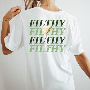 May include: White t-shirt with the text "FILTHY" repeated four times in green and black lettering. A green martini glass with an olive is centered on the shirt.