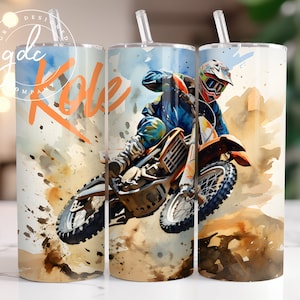 May include: A watercolor-style illustration of a motocross rider in a blue and orange jumpsuit, helmet, and goggles, jumping a dirt bike over a dirt track. The background is a watercolor wash of brown, orange, and yellow. The text "Kole" is written in orange on the tumbler.