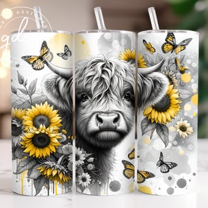May include: A white tumbler with a black and white illustration of a Highland cow with yellow sunflowers and butterflies. The tumbler has a clear lid and a straw.