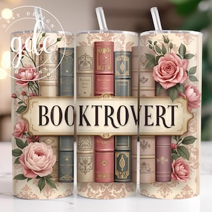 以下が含まれることがあります： ヴィンテージの本、バラ、そして「Booktrovert」という文字がデザインされた白いタンブラーです。