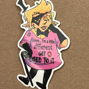 May include: A cartoon character with yellow hair, a black top hat, and a pink shirt with the text "Umm... I'm a little different get used to it".