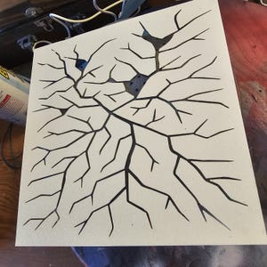 May include: A square, off-white panel with a black, branching pattern resembling cracks or veins. The design has a textured appearance, with a few dark blue accents. The overall aesthetic is abstract and artistic.