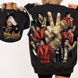 Könnte beinhalten: Schwarzes Sweatshirt mit einer Collage von Bildern von Michael Jackson, einem funkelnden Peace-Zeichen und einem goldenen Mikrofon. Auf der Vorderseite befindet sich ein Porträt von Michael Jackson mit dem Namen "Michael" in goldener Schrift.