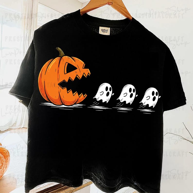 以下が含まれることがあります： ハロウィーンをテーマにしたグラフィックが特徴の黒いTシャツ。 ギザギザの口をしたオレンジ色のジャック・オ・ランタンが、3つの白い幽霊を追いかけています。 このデザインは、古典的なハロウィーンのテーマを遊び心たっぷりに表現しています。