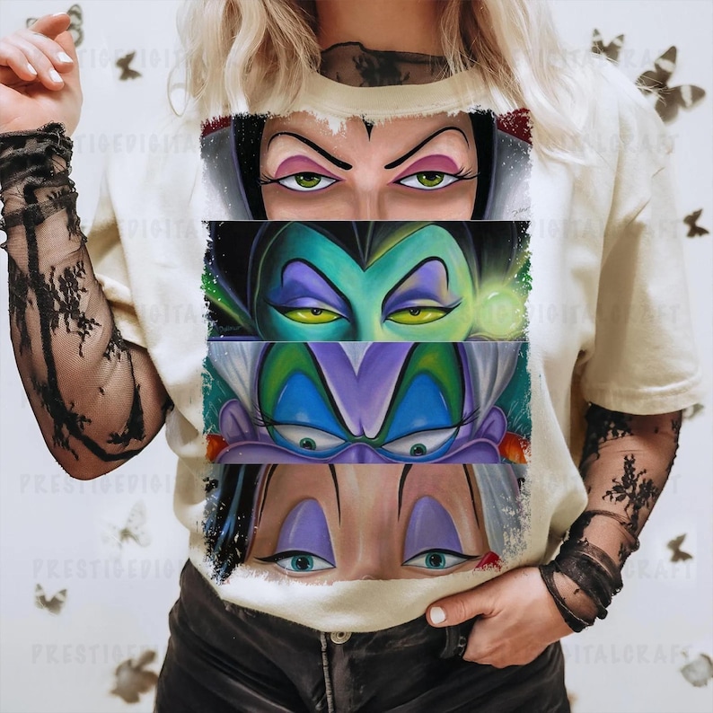 May include: Cream-colored t-shirt featuring a graphic of four sets of cartoon villain eyes. The eyes are in rectangular panels, each with a different color scheme. The shirt is worn by a person with black lace sleeves.