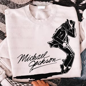 K&ouml;nnte beinhalten: Ein hellbeige Sweatshirt mit einer schwarzen Grafik von Michael Jackson in einer charakteristischen Tanzpose. Die Worte "Michael Jackson" sind in einer stilvollen Schriftart darunter geschrieben.