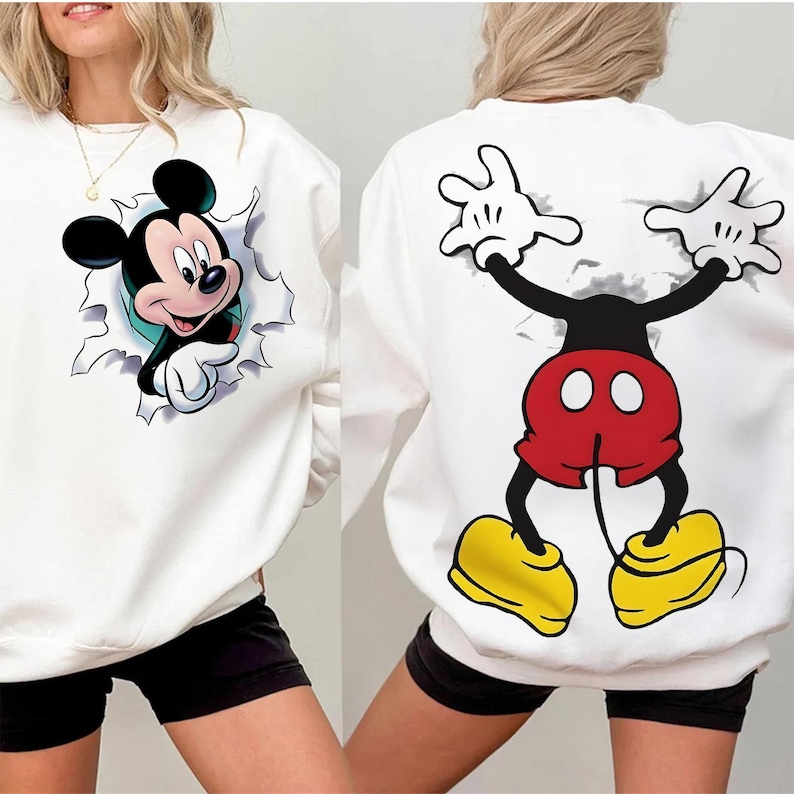 Op de afbeelding: Witte sweatshirt met Mickey Mouse-ontwerp. De voorkant toont Mickey die door een gescheurd gedeelte breekt, de achterkant toont Mickey's lichaam, armen en handen. Mickey's broek is rood, schoenen geel en handschoenen wit.