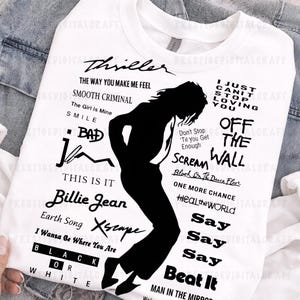 K&ouml;nnte beinhalten: Wei&szlig;es Sweatshirt mit einer schwarzen Silhouette eines T&auml;nzers und Songtiteln. Texte beinhalten "Thriller", "Billie Jean" und "Beat It". Das Sweatshirt befindet sich auf einem Jeans-Hintergrund.