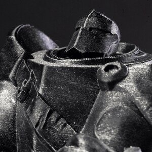 May include: A black and silver 3D printed robot figurine with a detailed helmet and textured surface.
