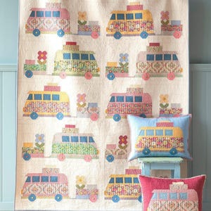 May include: A colorful quilt and two throw pillows featuring a repeating pattern of vintage-style camper vans. The vans are in shades of pink, yellow, and green, with floral and patterned details. The pillows are blue and red.