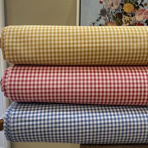 May include: Three rolls of gingham fabric in different colors: yellow, red, and blue. The fabric has a small checkered pattern.