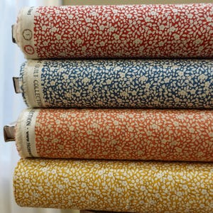 Könnte beinhalten: Vier Rollen Stoff mit einem weißen Blumenmuster auf rotem, blauem, orangefarbenem und gelbem Hintergrund. Der Stoff ist mit "Quilt Collection" gekennzeichnet.