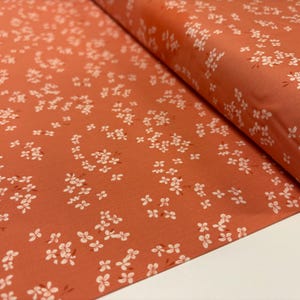 May include: A close-up of a coral-colored fabric with a white floral pattern. The fabric is folded and the pattern is visible on both sides.