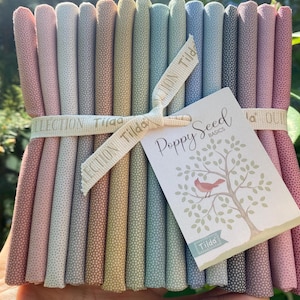 May include: A bundle of rolled fabric in various pastel colors, including pink, green, and blue, tied with a ribbon that reads "Collection Tilda." A tag with the text "Poppy Seed Basics" and a tree illustration is attached.