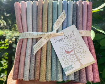 May include: A bundle of rolled fabric in various pastel colors, including pink, green, and blue, tied with a ribbon that reads "Collection Tilda." A tag with the text "Poppy Seed Basics" and a tree illustration is attached.