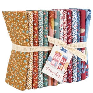 Puede incluir: Una pila de cuadrados de tela doblados de la colección Tilda Quilt, atados con una cinta de marca y una etiqueta que dice Village Life. Los textiles presentan varios patrones florales, de hojas y arquitectónicos en tonos mostaza, rojo, azul y blanco.