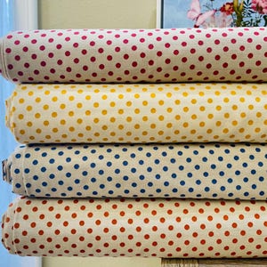 May include: Four rolls of fabric with a white background and different colored polka dots. The fabric rolls are stacked on top of each other. The top roll has pink polka dots, the second roll has yellow polka dots, the third roll has blue polka dots, and the bottom roll has orange polka dots.