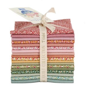 May include: A stack of colorful fabric squares, featuring various floral patterns in shades of red, pink, green, and yellow. The fabric is tied with a cream-colored ribbon that reads "Tilda Quilt Collection". A tag with a floral design is attached.