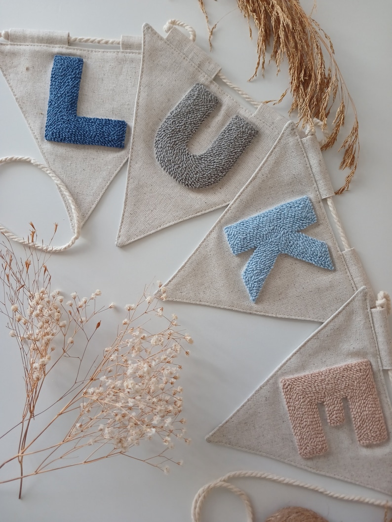 May include: A banner with the name "LUKE" spelled out in colorful yarn letters. The letters are sewn onto triangular fabric flags. The flags are connected by a white string.