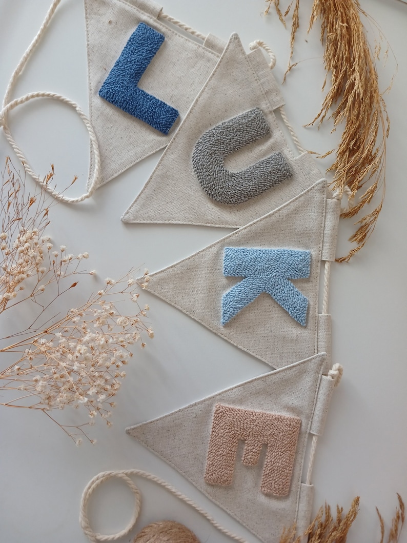 May include: A banner with the name "LUKE" spelled out in colorful yarn letters. The letters are attached to triangular fabric flags with a white background. The banner is strung together with white twine.