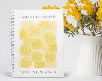 May include: A white spiral-bound student planner with the name "SAMANTHA JOHNSON" at the top. The cover features a pattern of yellow lemon slices. The words "STUDENT PLANNER" are at the bottom. A white pitcher holds yellow flowers.