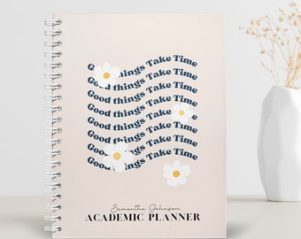 May include: A beige academic planner with a spiral binding. The cover features a white daisy design and the text "Good things take time" repeated in a circular pattern. The planner also includes the name "Samantha Johnson" and the words "Academic Planner".