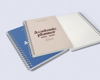 May include: A beige academic planner with a brown title "Academic Planner 2024-2025" and a small illustration of an open book. The planner is closed and stacked on top of a blue spiral bound notebook.