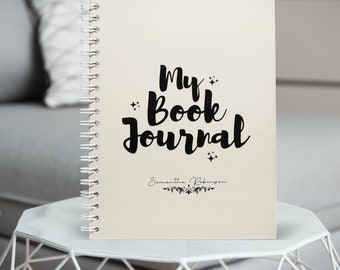 May include: A cream-colored spiral bound journal with the text "My Book Journal" in black cursive font. The name "Samantha Robinson" is written in black cursive font below the title.