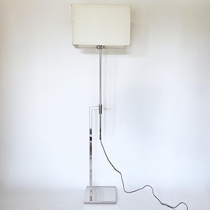 May include: A chrome floor lamp with a white rectangular lampshade. The lamp has a long, thin stem and a square base.