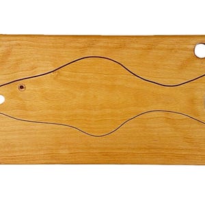 Puede incluir: Una tabla de cortar de madera de color claro con un diseño de pez. El contorno del pez es de color marrón oscuro y la tabla tiene un agujero en la esquina superior derecha. El ojo del pez es un pequeño círculo oscuro.