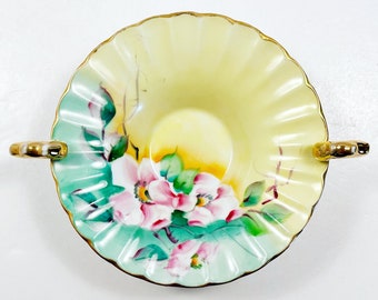 May include: A vintage porcelain bowl with two gold handles. The bowl is decorated with a floral design of pink and white flowers with green leaves on a light blue and yellow background.