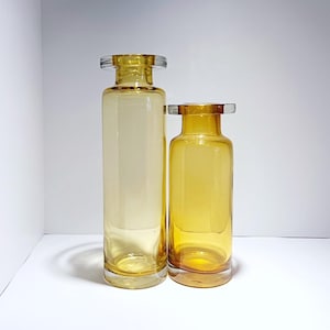 Op de afbeelding: Twee amber glazen vazen, een groter dan de andere, met een heldere glazen bovenrand.