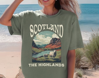 May include: A green t-shirt with a vintage-style illustration of a Scottish landscape with sheep and the text "Scotland The Highlands".
