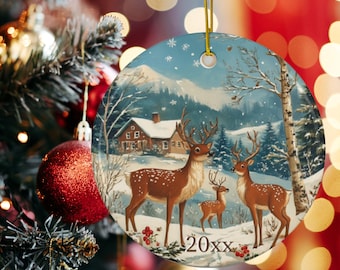 May include: Round Christmas ornament featuring a winter scene with deer, a house, and snow-covered mountains. The ornament has a gold string for hanging and the year "20xx" is printed on the bottom.