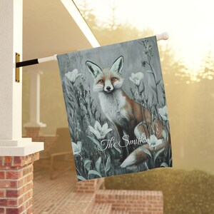 May include: A garden flag with a watercolor painting of a fox in a field of white flowers. The text "The Smiths" is written in cursive at the bottom of the flag.