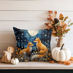 May include: A decorative throw pillow with a blue background featuring two foxes and a full moon. The foxes are orange and white with black noses and eyes. The moon is white with a yellow glow. The pillow is surrounded by a border of small white flowers.