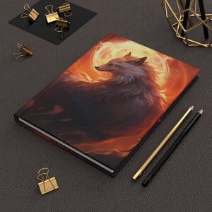May include: A hardcover journal with a colorful illustration of a wolf in a fiery orange and yellow background. The wolf is facing to the right and has a white ring around it.