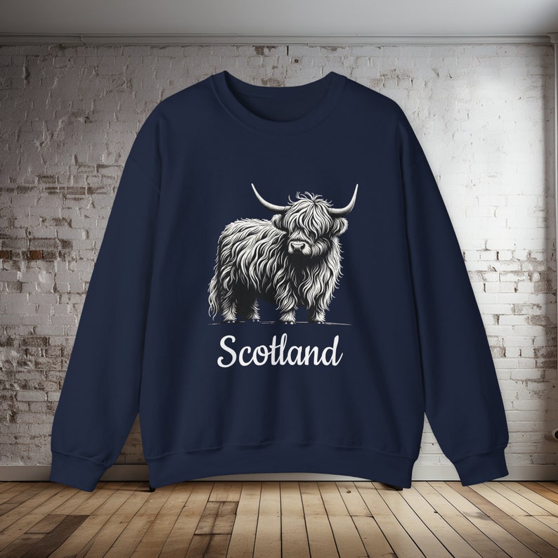 Puede incluir: Una sudadera azul marino con un gr&aacute;fico blanco de una vaca de las tierras altas y la palabra "Escocia" impresa debajo.