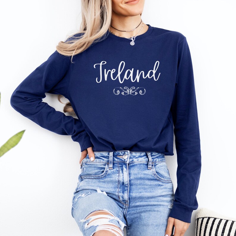 May include: A navy blue long-sleeved shirt with the word "Ireland" printed in white script on the front. The shirt has a relaxed fit and a crew neckline.