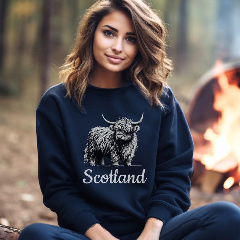 Puede incluir: Una sudadera azul marino con un gr&aacute;fico blanco de una vaca de las tierras altas y la palabra "Escocia" debajo.