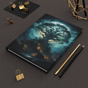 May include: A dark blue notebook with a full-color illustration of a large, gnarled tree with glowing lights in the branches. The tree is silhouetted against a full moon and a dark, starry sky.