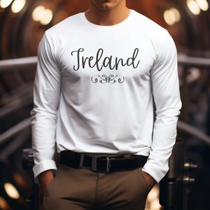 May include: White long-sleeve t-shirt with the word "Ireland" printed in black cursive lettering with a decorative flourish underneath.