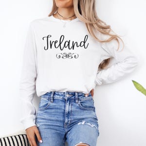 May include: White long-sleeve t-shirt with the word "Ireland" in black script lettering and a decorative flourish.