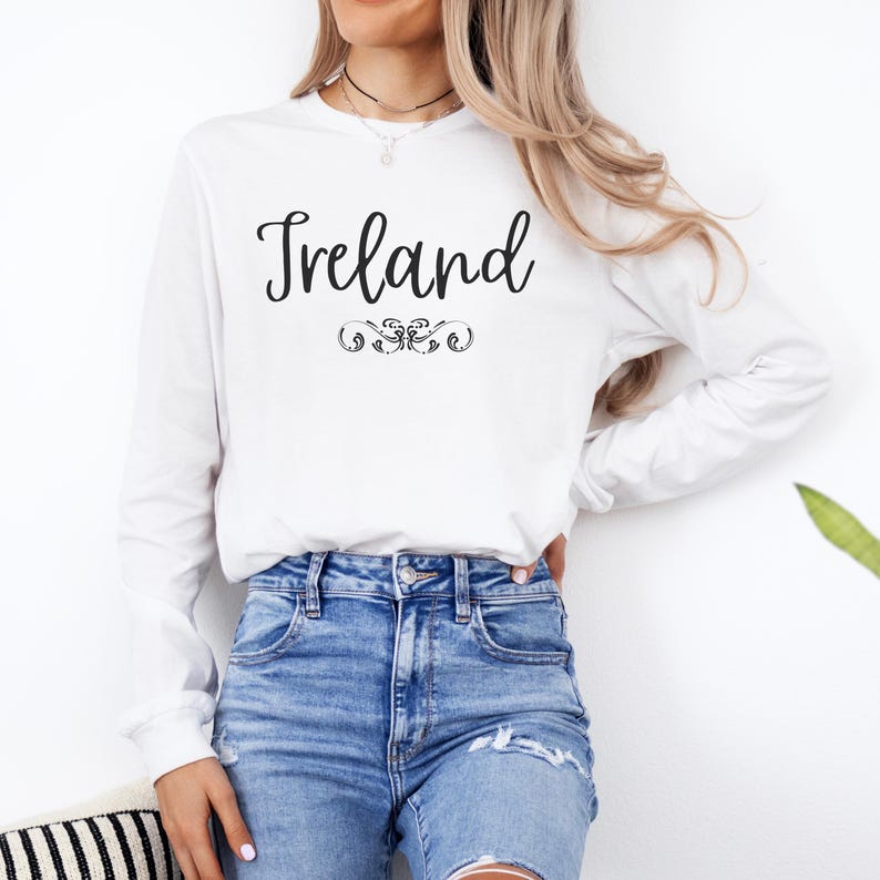 May include: White long-sleeve t-shirt with the word "Ireland" in black script lettering and a decorative flourish.