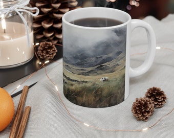 May include: White ceramic mug with a scenic image of a misty mountain landscape with sheep grazing in a field. The mug is filled with a dark liquid, likely coffee or tea.