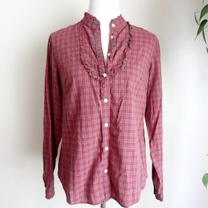 May include: A red and black checked long-sleeved button-up shirt with a frilled collar.