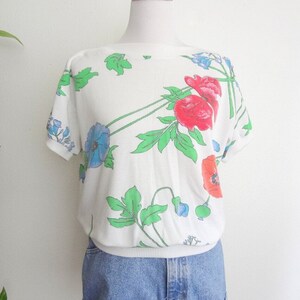 May include: White short-sleeved shirt with a floral print featuring red, blue, and green flowers.