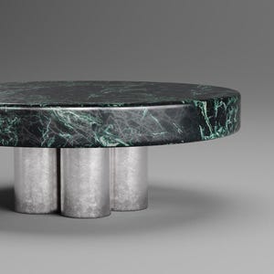 May include: A round coffee table with a dark green marble top and three silver cylindrical legs. The marble has a natural veining pattern in shades of green and white. The table is a modern design.